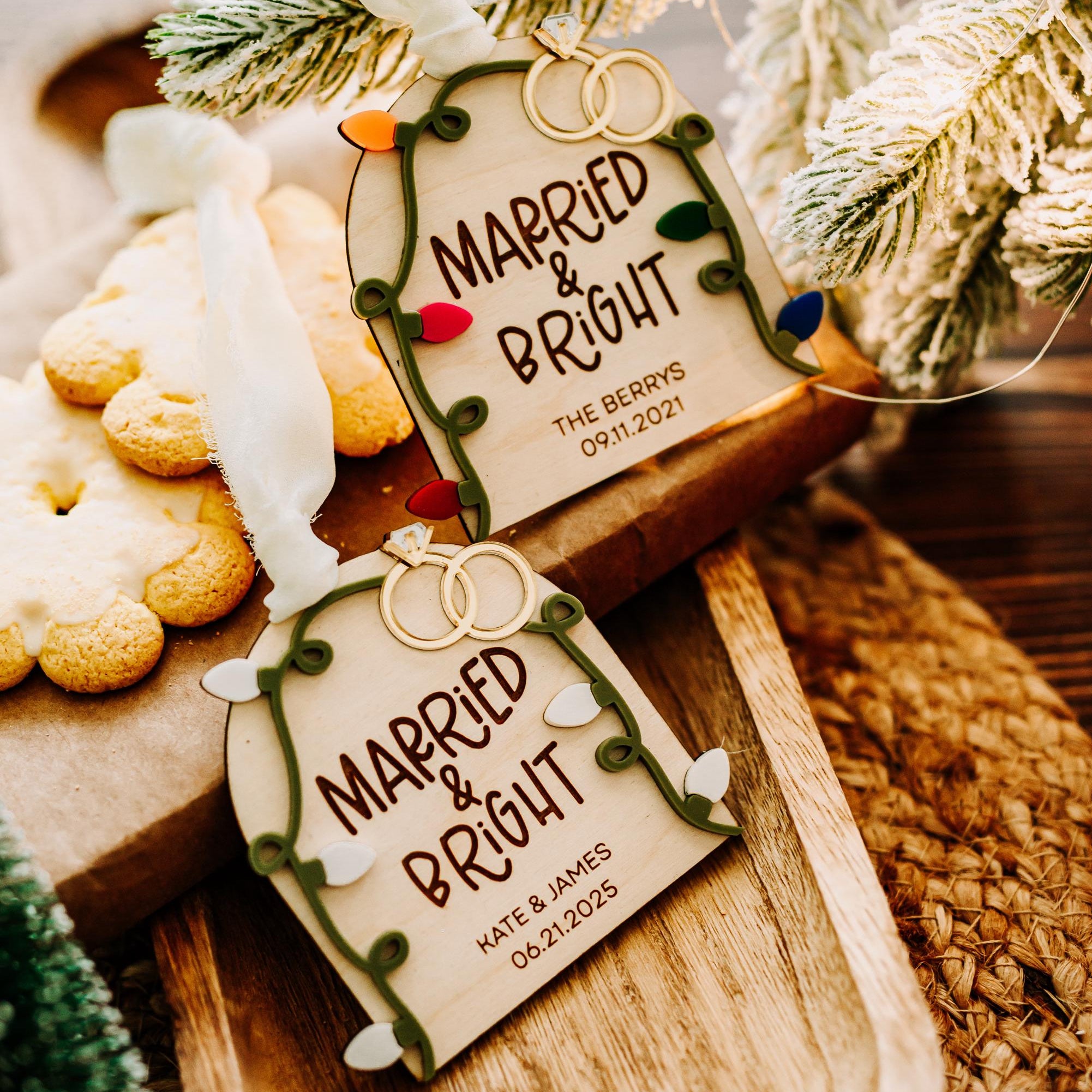 Two personalized Christmas ornament tags reading 'MARRIED & BRIGHT' with gold wedding rings printed at the top, styled on a wooden board with cookies, evergreen branches, and a woven textile.
