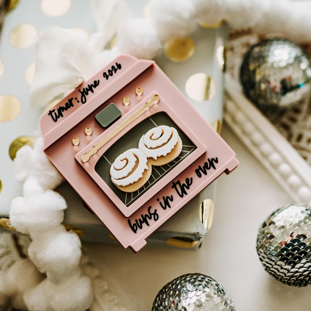 A pink oven shaped ornament, styled on a white tray with gold polka dots, white fluffy garland, and silver disco balls.