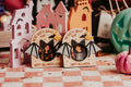 Two Halloween-themed wooden arch-shaped photo magnets with bat wings and circular cutouts, displayed on a checkered tablecloth with other seasonal decor in the background.