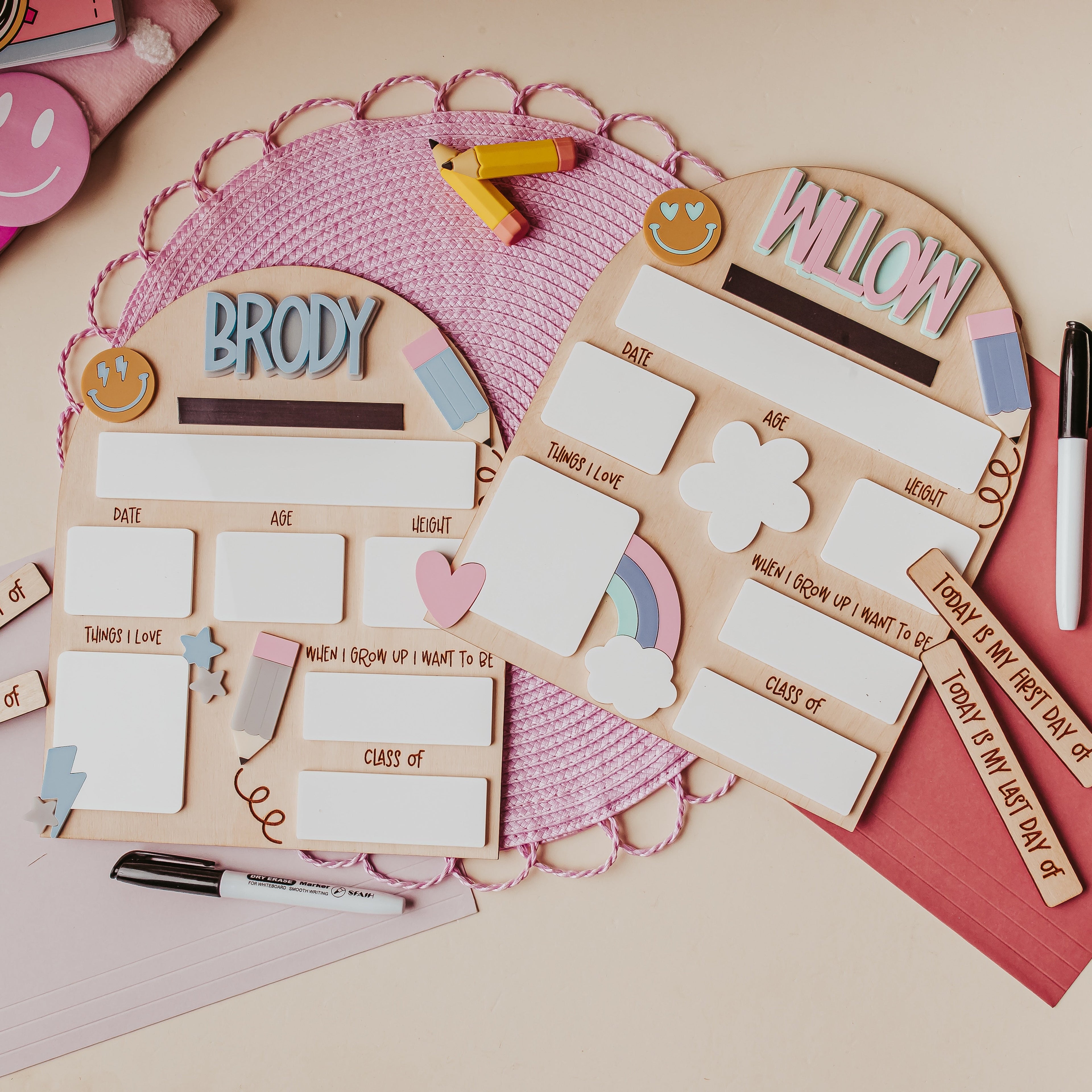 A styled flat-lay of two personalized woodendry erase back to school boards with blank boxes, stickers, markers, and smiley-face cards on a beige surface.