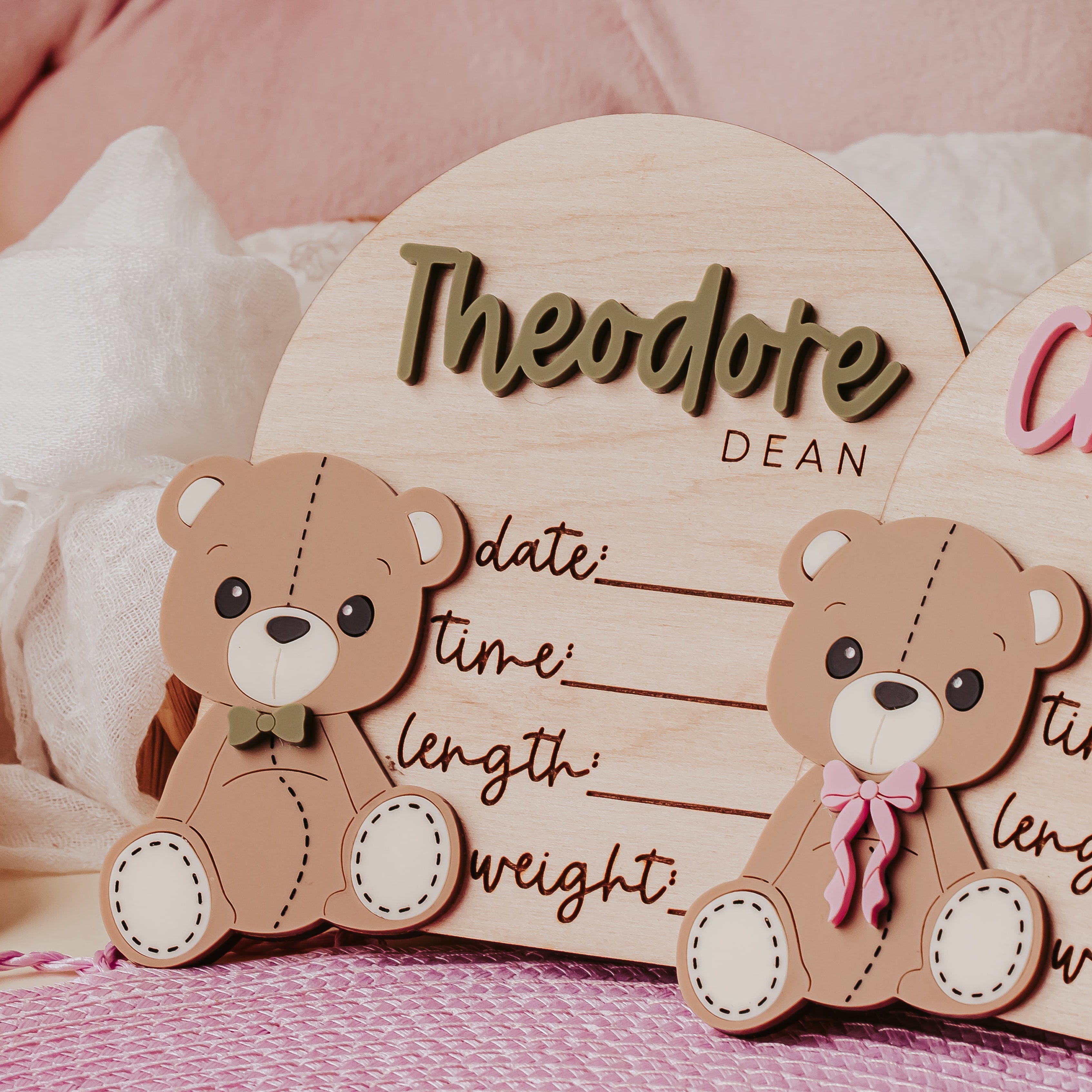 Two personalized wooden baby birth stat signs shaped as an arch with  teddy bears, with the name Theodore  visible and set against a soft pink and white baby-themed background.