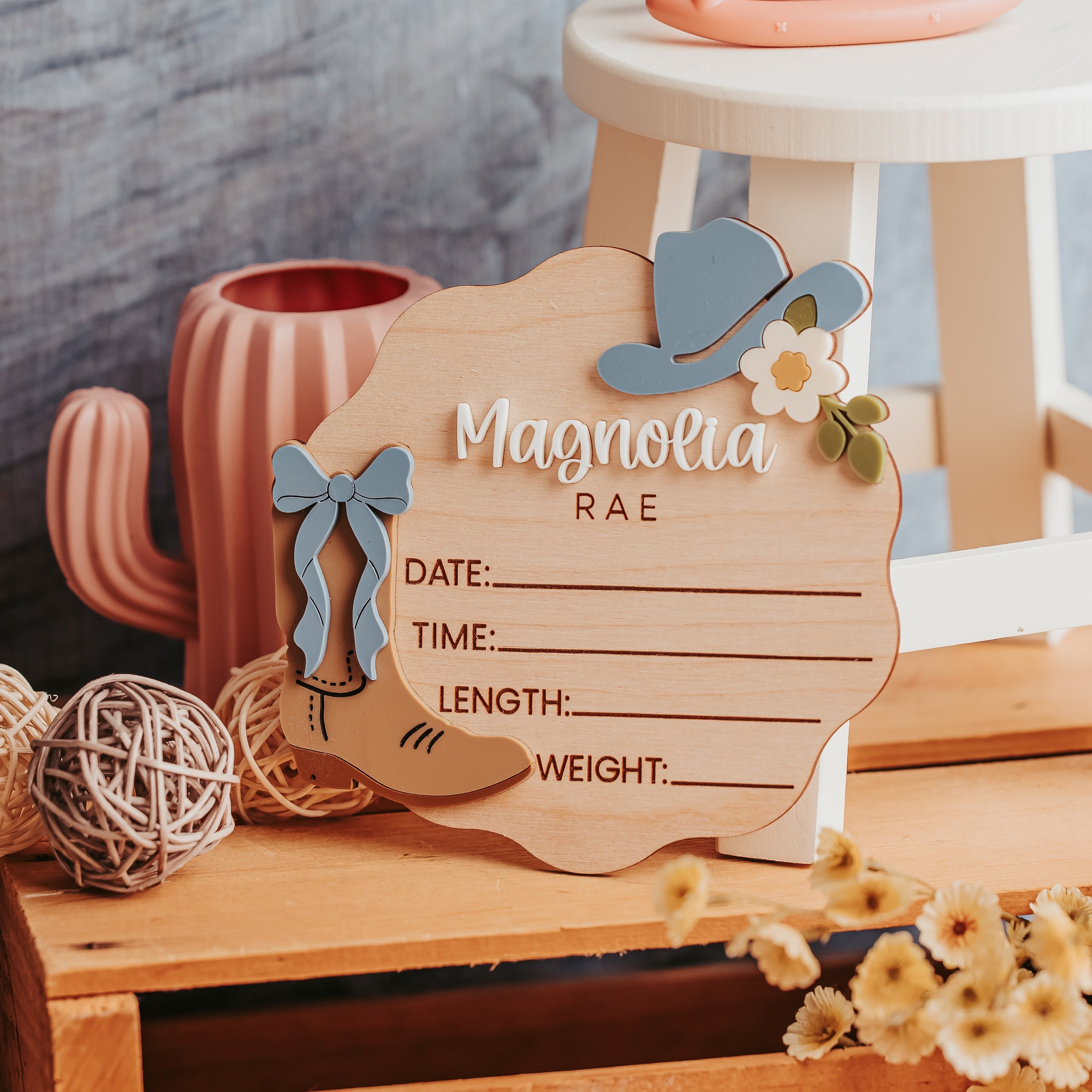 A wooden baby birth stat with a western theme, featuring a cowboy hat, bow, and floral accents, styled on a rustic wooden crate with decorative props.