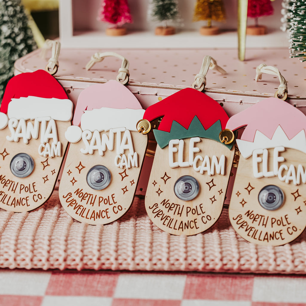 Four Christmas-themed faux camera tags Santa and Elf hats that read 'SANTA CAM', 'ELF CAM' and north pole surveillance 