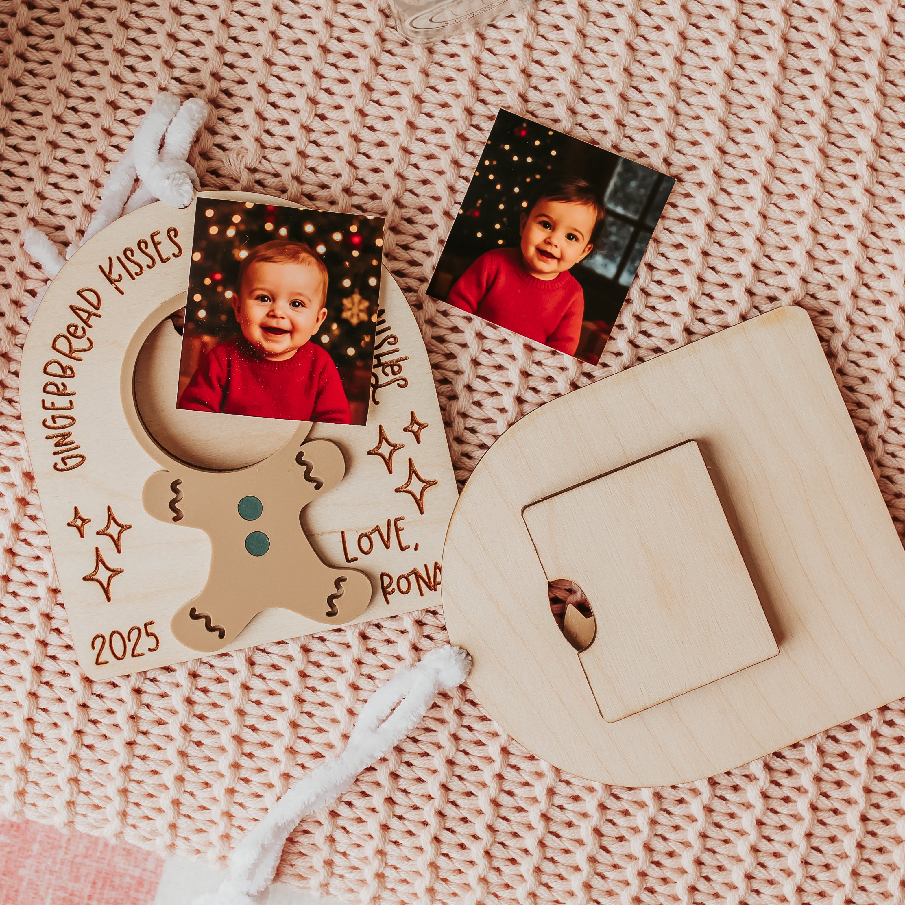 A wooden personalized photo frame ornament and matching wooden display stand arranged on a pink knit blanket, with two printed child photos placed beside them.