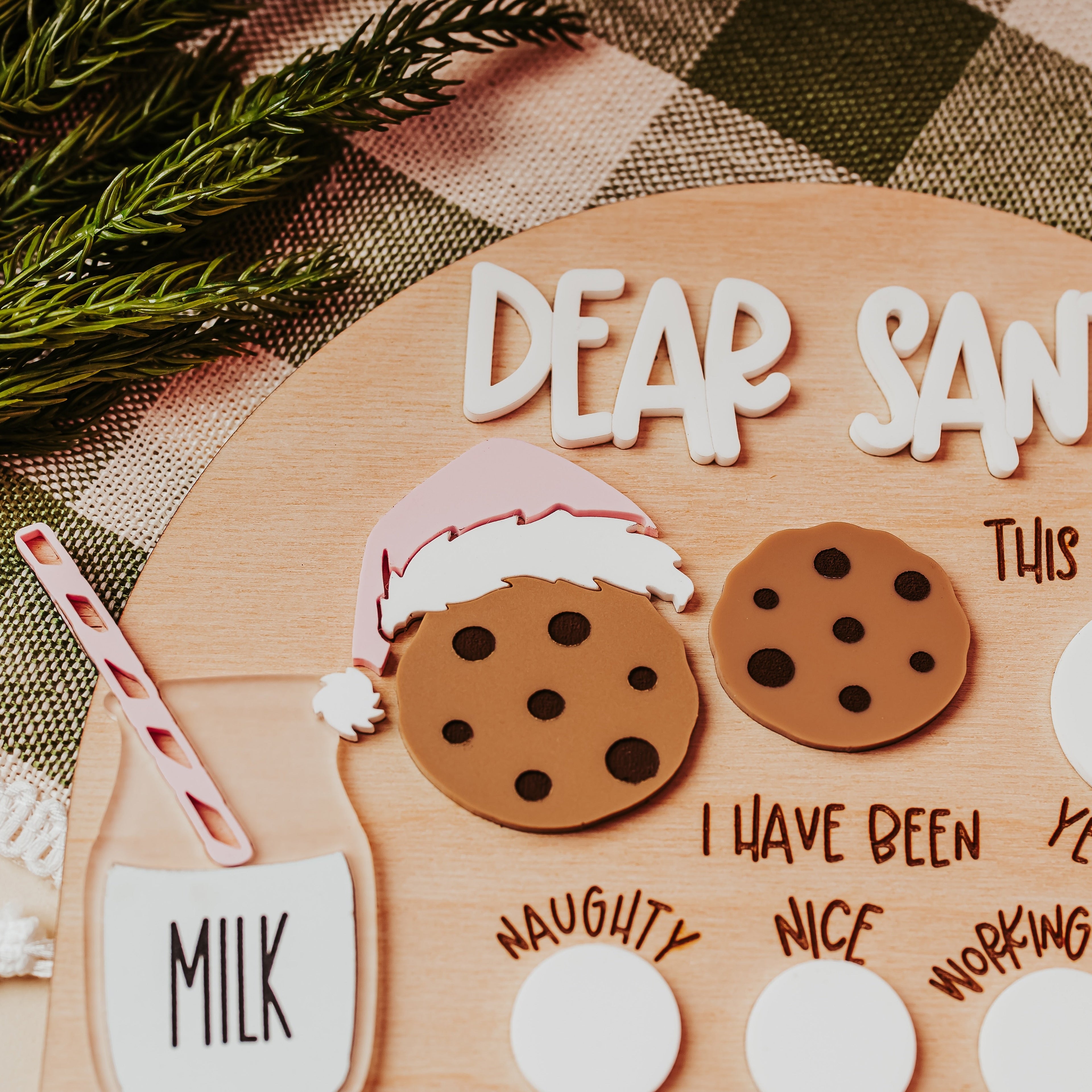 A festive handmade Christmas letter to Santa displayed on a wooden board. The kit includes white foam letters spelling 'DEAR SANTA', two brown cookie cutout shapes with black polka dots, a pink and white Santa hat, a milk cup with a red-and-white striped straw, and blank white oval stickers for personalization.