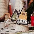 A personalized wood and acrylic Christmas ornament featuring an excavator and tree silhouette with the name 'JENSEN' and the year '2025', displayed on a decorated holiday table.