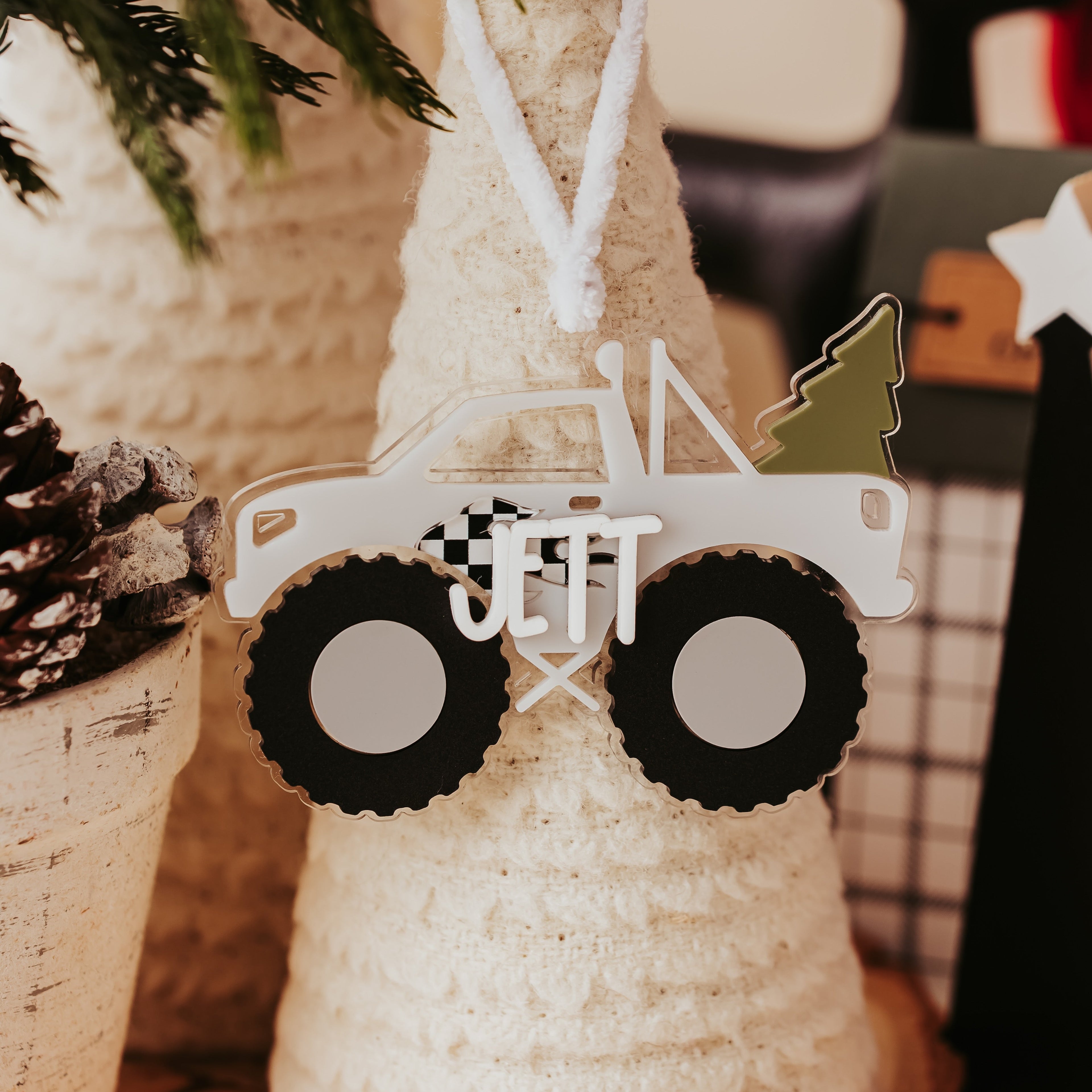 A personalized Christmas ornament shaped like a monster truck with black wheels and the name 'JETT' in the cargo area, a tree