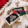 Two chalkboard Christmas ornaments on a cream and gold colored gift box. One chalkboard ornament has an apple with a bite missing and a worm coming out of it. The other chalkboard ornament has a stack of books with the year and 'ABC' at the top.