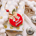 A red apple-shaped teacher Christmas ornament with a gold bow and the words 'Mrs. Johnson' in white script, resting on a wrapped gift box with gold polka dots